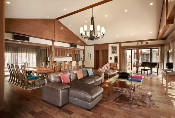 A spacious living room with a large sectional sofa, a dining area with a wooden table and chairs, a piano, and a chandelier. - Onsen At Moncham (Mae Rim)