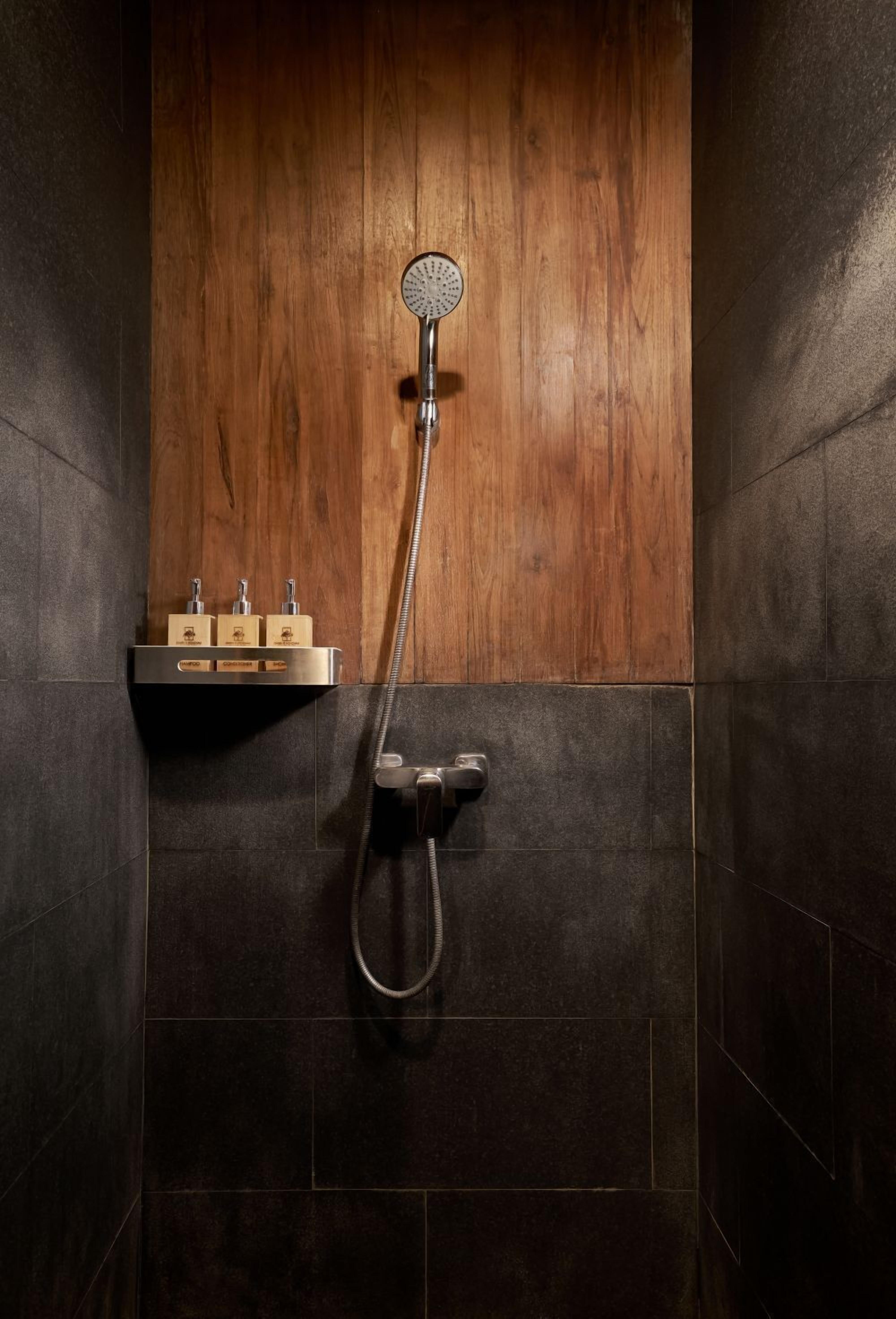 Une douche avec un mur en panneaux de bois, un pommeau de douche à main et un robinet fixé au mur.