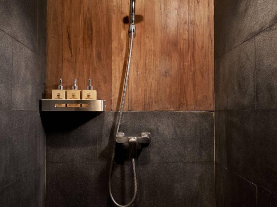 Une douche avec un mur en panneaux de bois, un pommeau de douche à main et un robinet fixé au mur.