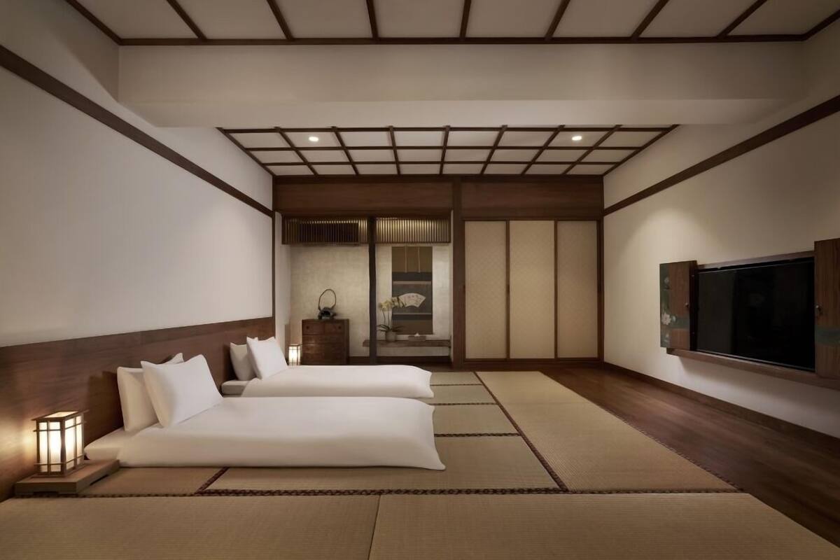 A hotel room with tatami flooring, a sofa, a TV, and a traditional Japanese sliding door.