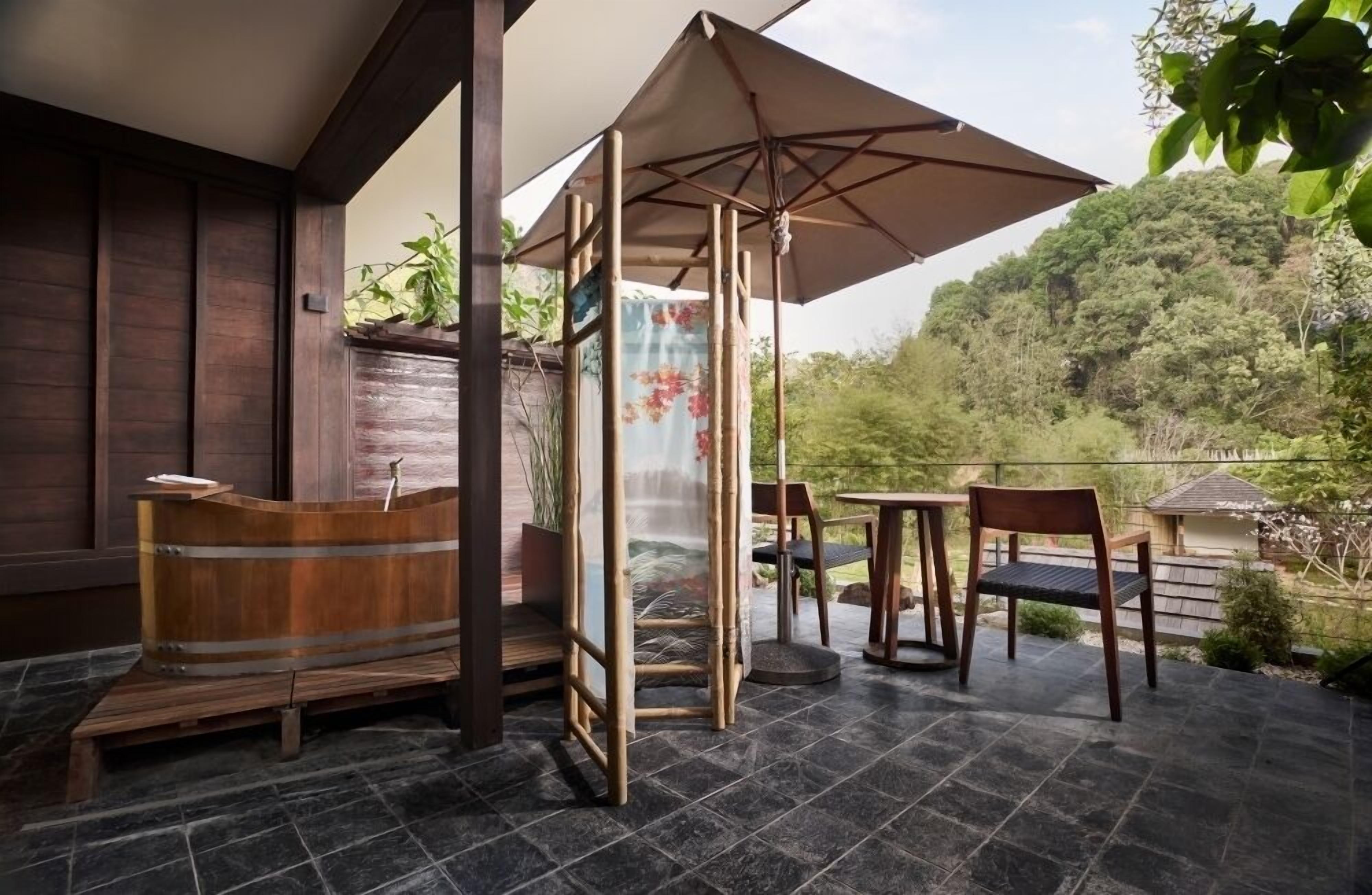 A wooden bench, a table, an umbrella, and a view of a forested hill.