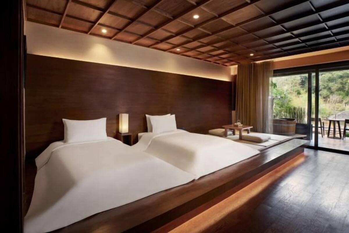 A double bed with a wooden headboard, bedside tables, and a view of the outdoors through a glass door.