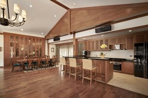 Una cocina amplia con armarios de madera, un comedor con una mesa grande y sillas, y una zona de bar con taburetes.