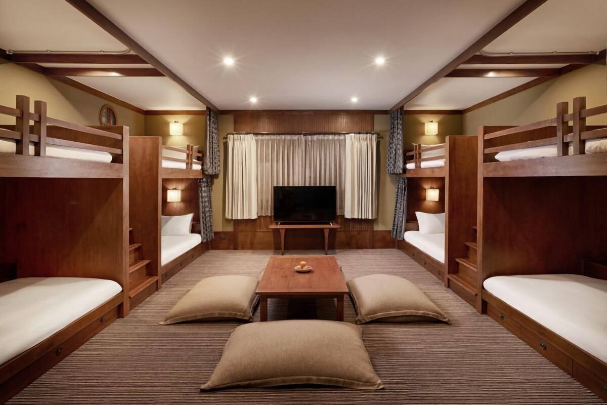 A room with bunk beds, a TV, and a central table with cushions.