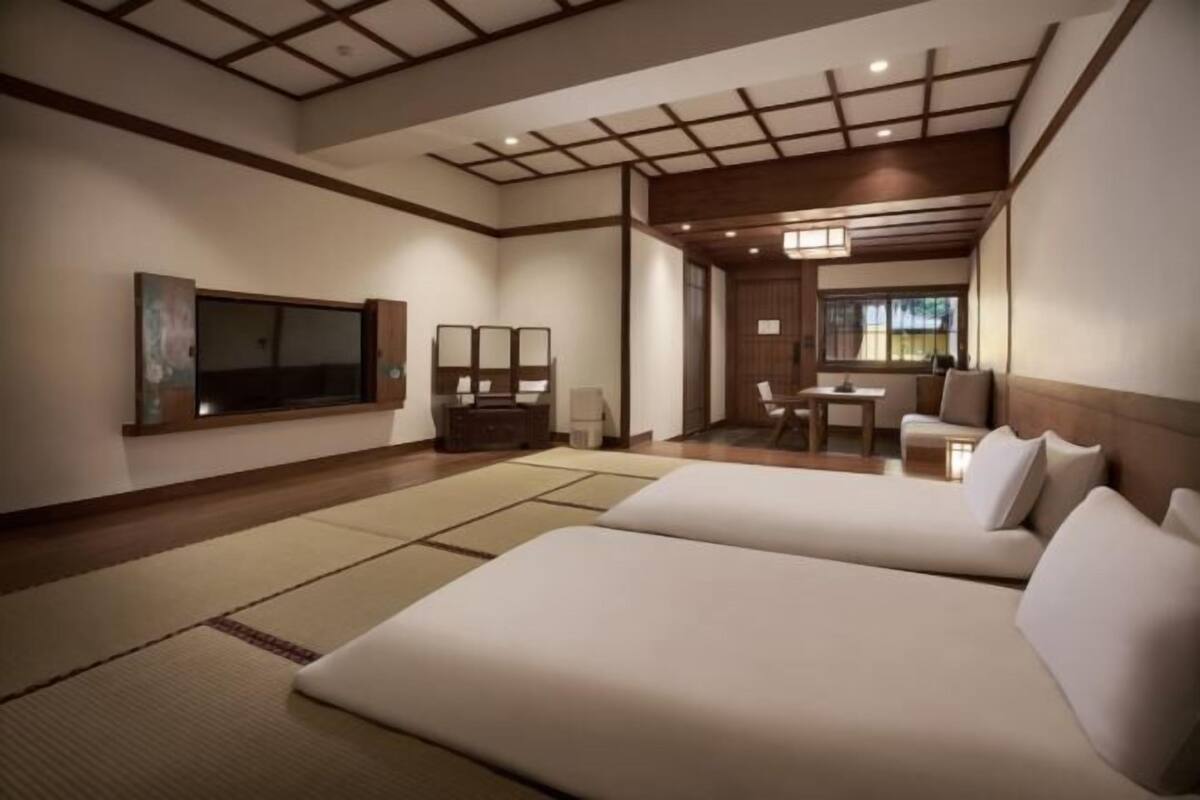 A hotel room with two beds, a desk, a chair, a TV, and a large window.