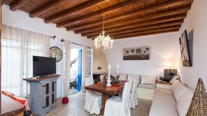 Una sala de estar acogedora con techo de madera, un televisor sobre un mueble bajo, una mesa de comedor con sillas y un sofá.