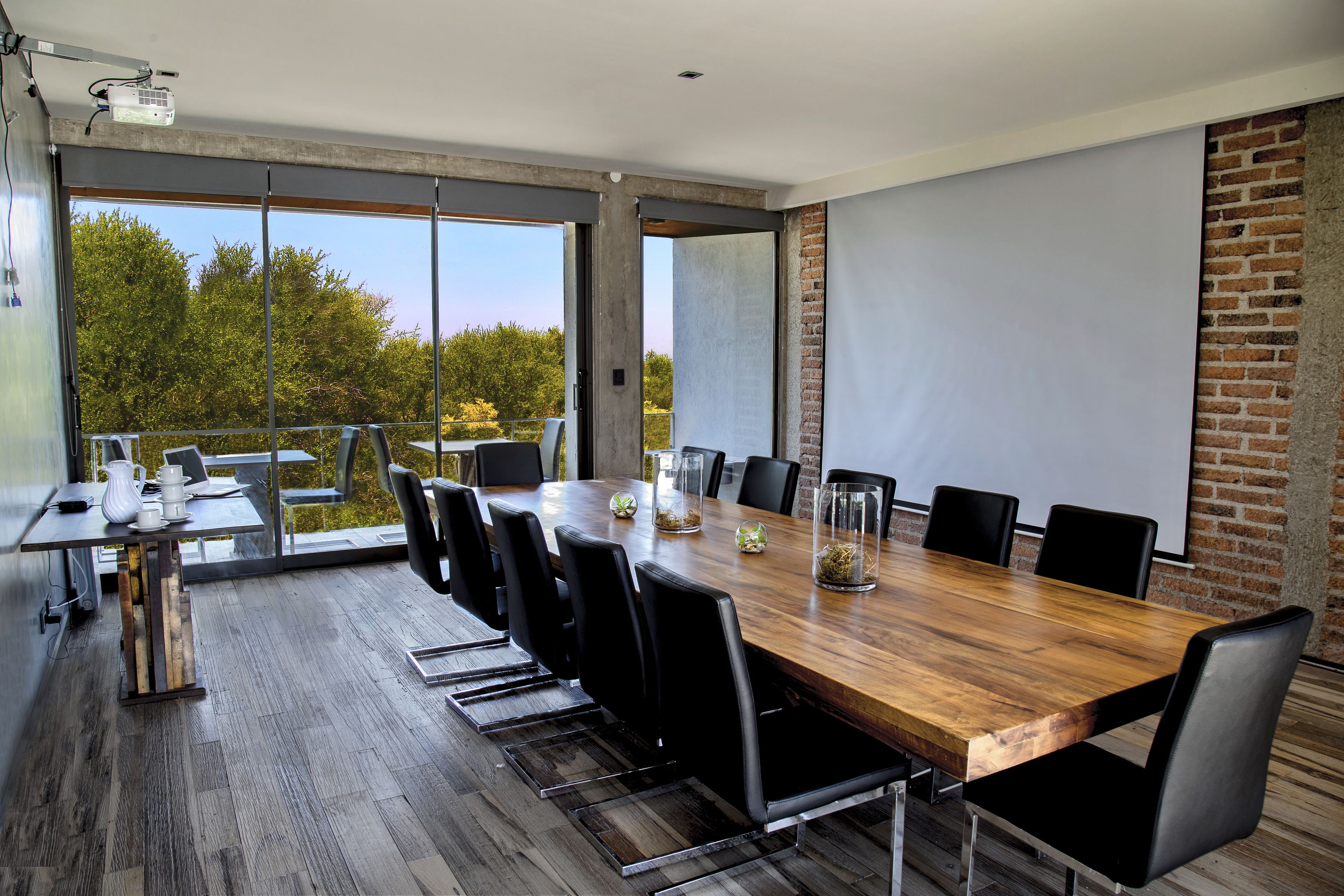 A conference room with a large wooden table, black chairs, and a projector screen.