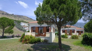 Una casa de dos pisos con balcón, rodeada de vegetación y un paisaje montañoso.