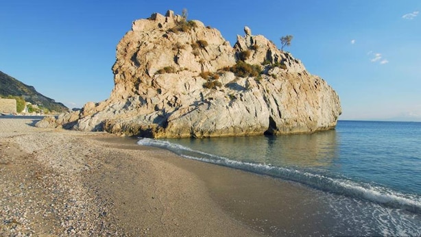 Una playa rocosa con una gran formación de roca y mar tranquilo.