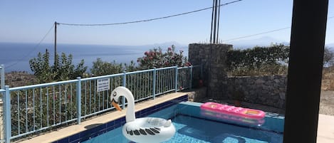 A swimming pool with a swan float, a stone wall, and a view of the sea.
