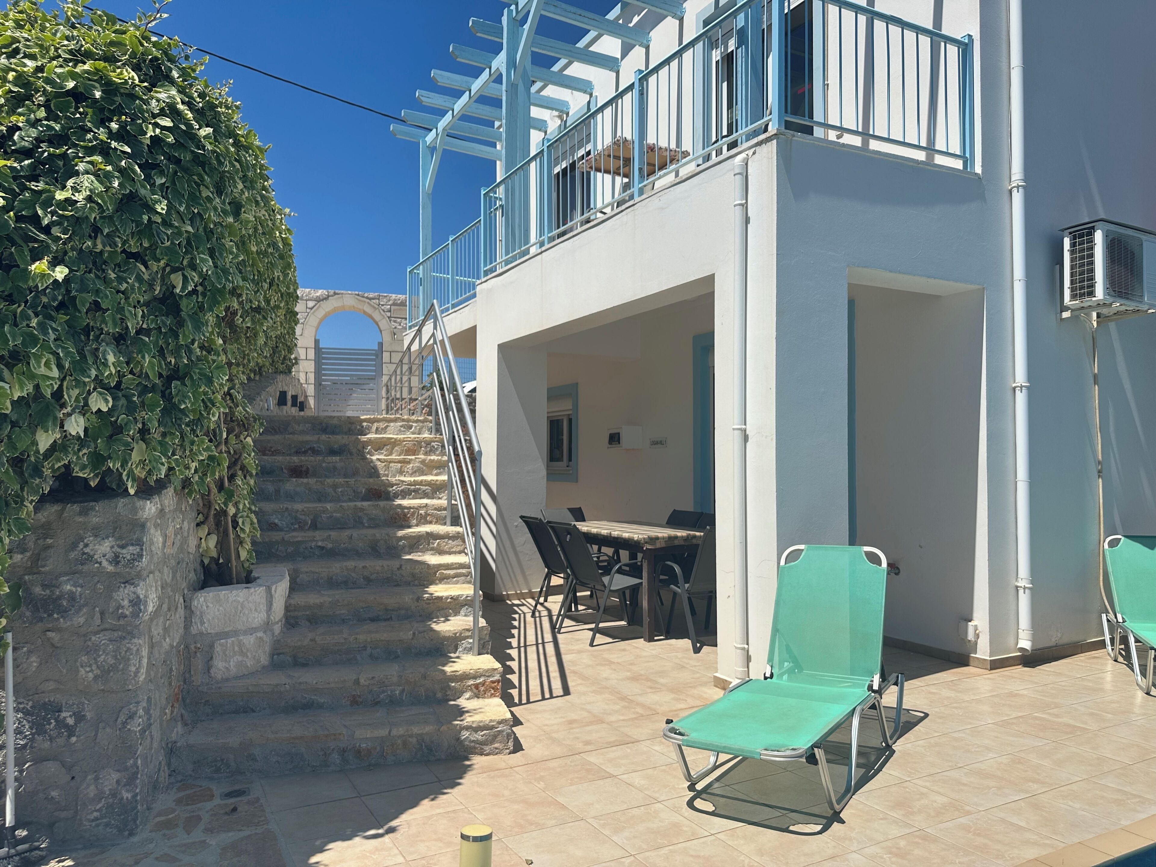A two-story building with a stone staircase, outdoor seating area, and a view of a gate in the background.