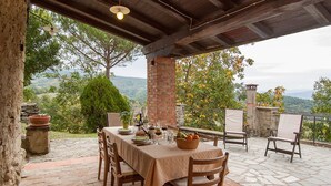Une terrasse extérieure avec une table dressée pour le repas, entourée d’un sol en pierre et de chaises en bois.