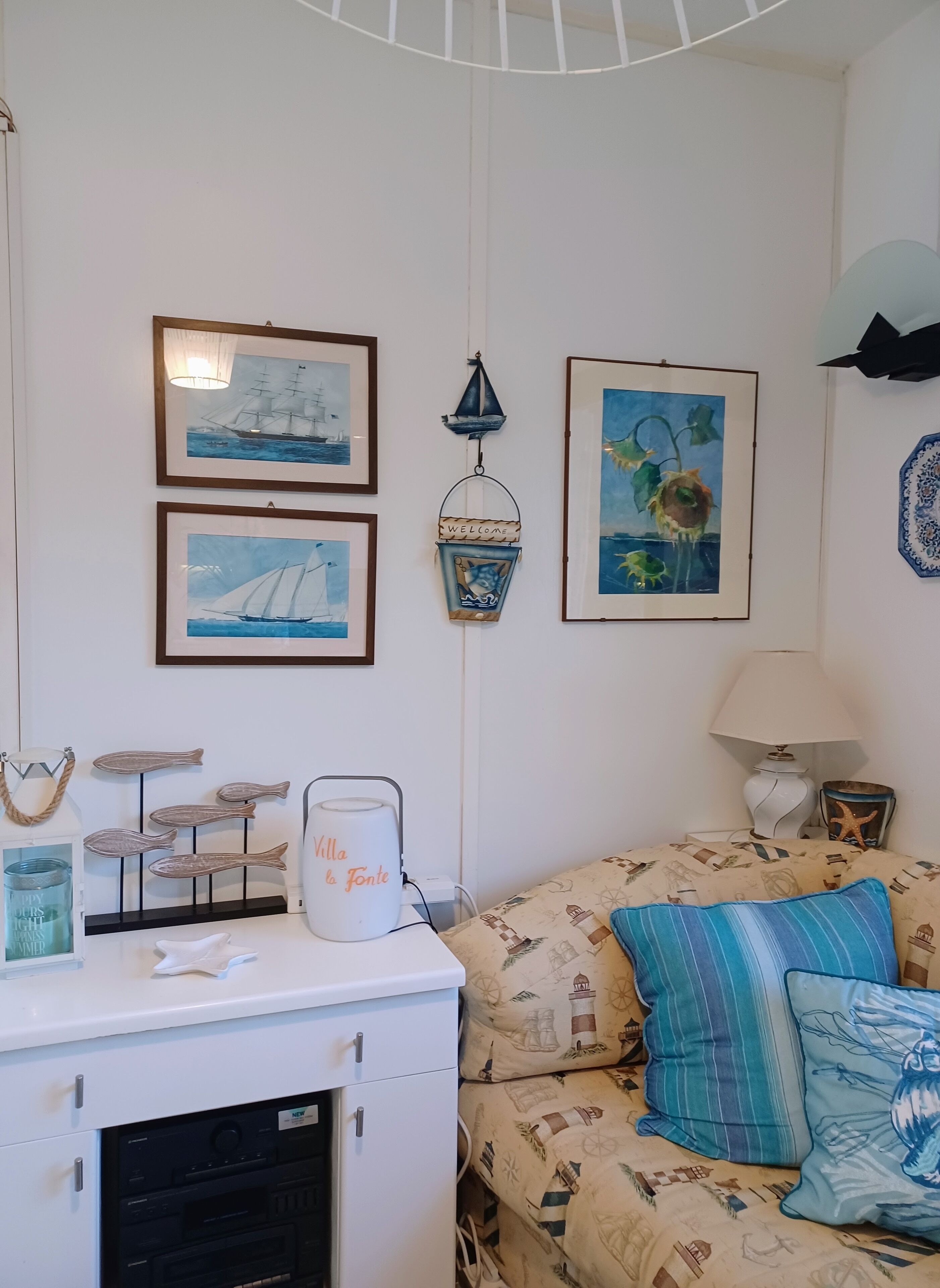 A room with a bed, a white cabinet, framed artwork, a lamp, and decorative fish on the wall.
