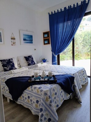 A neatly made bed with a floral bedspread, a tray with two mugs and a teapot, and a blue curtain.