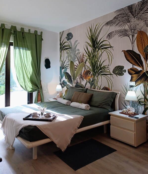 A bedroom with a bed, nightstands, a window with curtains, and a tropical-themed wall mural.