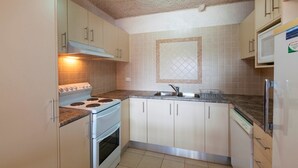 A compact kitchen with white cabinets, a stove, and a microwave. - Central Park 4 - Centre of Jindabyne (Jindabyne)