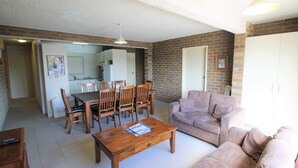 A living room with a wooden coffee table, a sofa, and a dining area with a table and chairs. - Central Park 4 - Centre of Jindabyne (Jindabyne)
