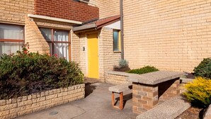 A brick building with a yellow door, a small outdoor seating area, and a window with a view of the sky. - Central Park 4 - Centre of Jindabyne (Jindabyne)