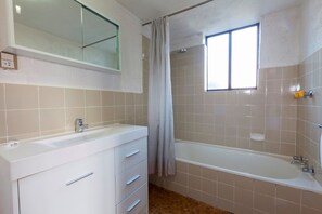 Une salle de bain avec un meuble-lavabo blanc, une baignoire et une fenêtre.