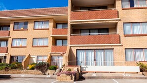 A multi-story brick building with balconies, a parking lot, and a small landscaped area with plants. - Central Park 4 - Centre of Jindabyne (Jindabyne)