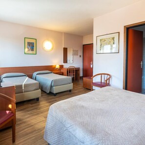 A hotel room with two single beds, a larger bed, a wooden chair, a desk, and a small table. - Albatros (CALENZANO)
