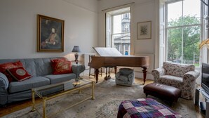 Una sala de estar con un piano de cola, un sofá, un sillón floral y un televisor.