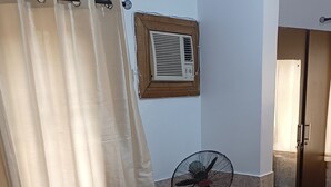 A room with a brown sofa, two black cushions, a standing fan, a window with a wooden frame, and a wall-mounted air conditioner. - Entire, spacious, furnished 3beds en-suite, as holiday let with BrausengDelight (Lagos)