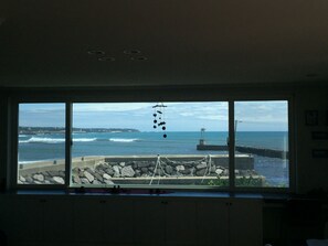 A room with a large window overlooking a rocky shoreline and the ocean.