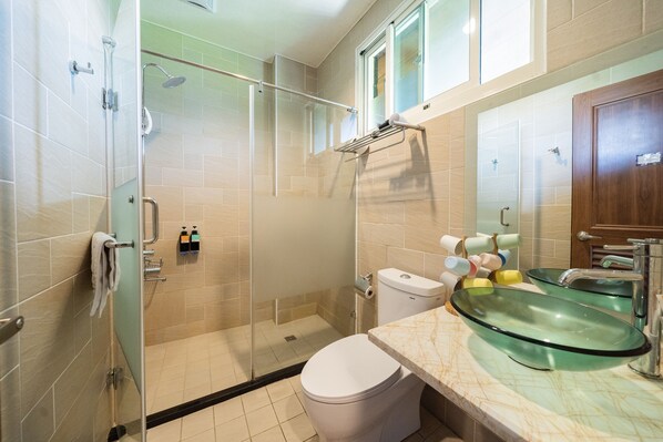 Un baño moderno con cabina de ducha de vidrio, inodoro, lavabo de vidrio y toallero.