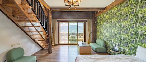 Una habitación con escalera de madera, cama, sofá verde, una mesita y vistas por un ventanal grande.