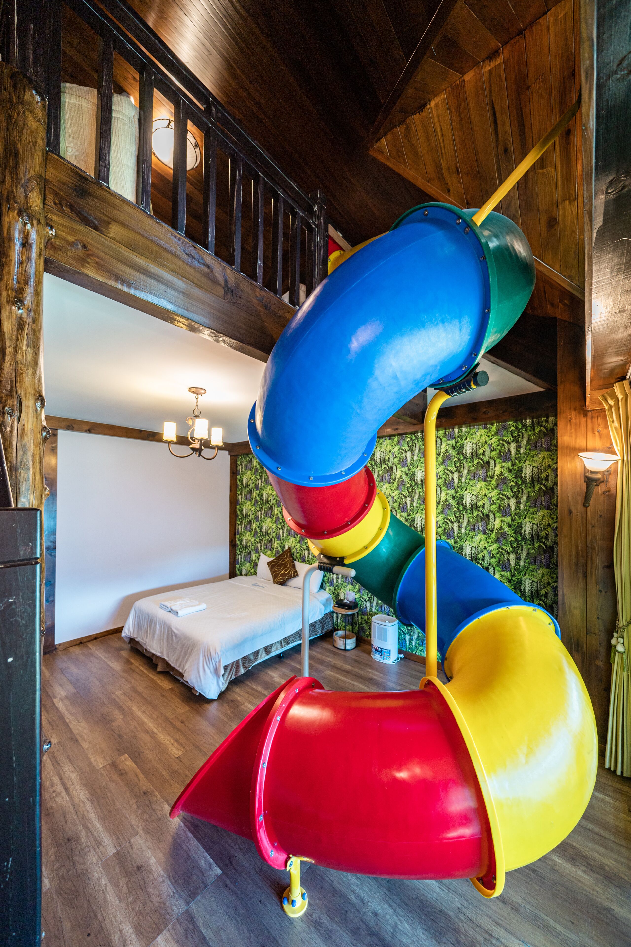 Un tobogán de varios colores en una habitación con paredes de madera y una cama.