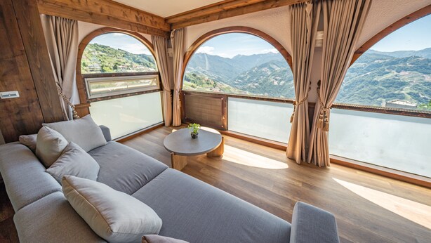 Un interior moderno con un sofá, una mesa redonda y ventanas amplias que ofrecen una vista panorámica de la montaña.