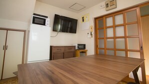 Una habitación con una mesa de comedor de madera, un microondas, un televisor y un mueble pequeño.
