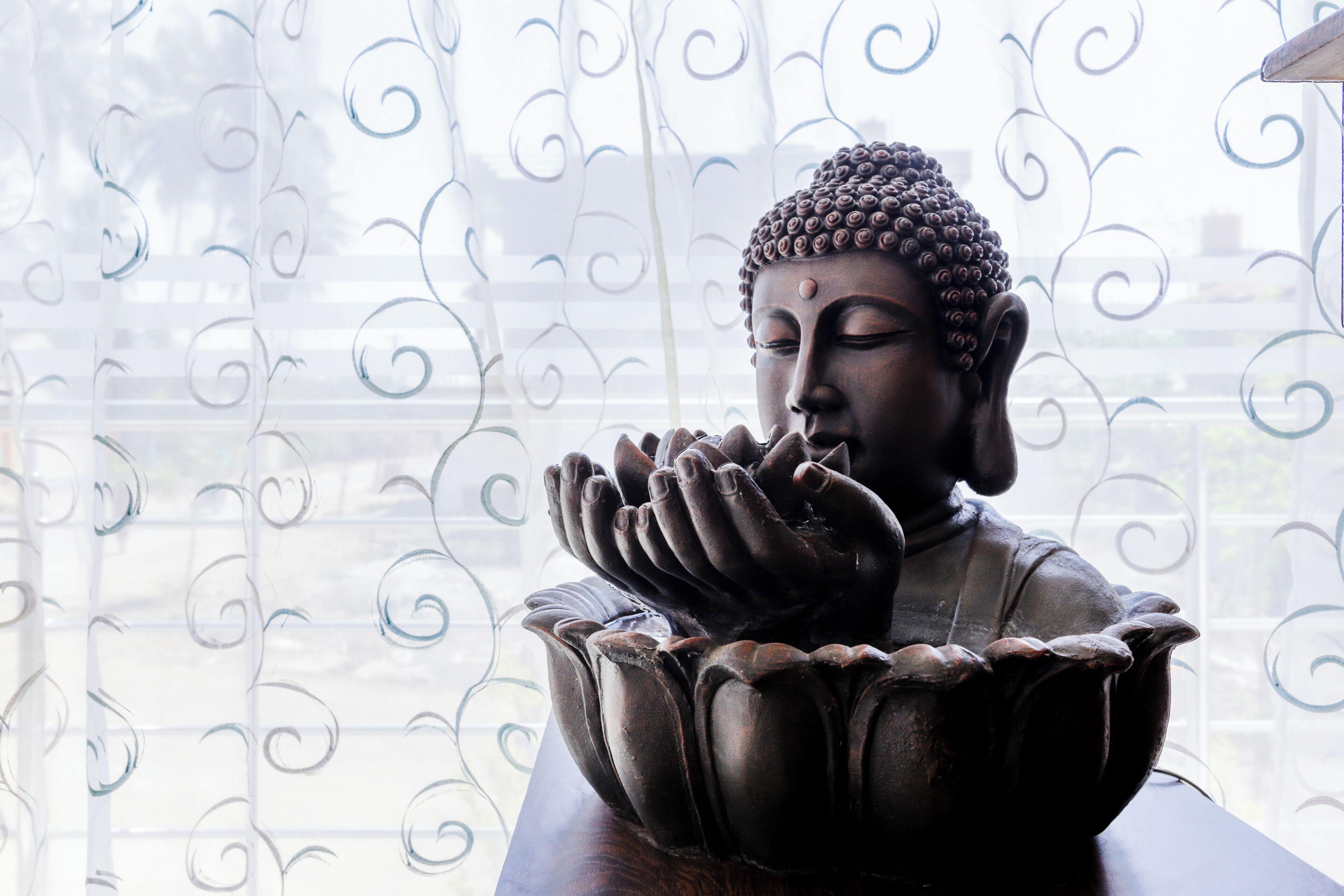 Une statue de Bouddha, les mains jointes en position de prière, est placée sur un socle en forme de lotus, devant une clôture décorative en métal.
