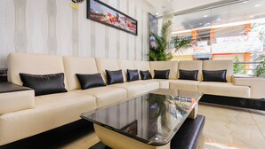 A modern hotel lobby with a beige sectional sofa, black cushions, a glass coffee table, and a large window with a view of the outside. - Treebo Sandpipers Kushalnagar (Somvarpet)