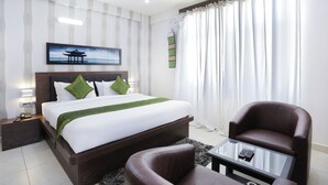 A hotel room with a bed, a chair, a glass coffee table, and a painting on the wall. - Treebo Sandpipers Kushalnagar (Somvarpet)