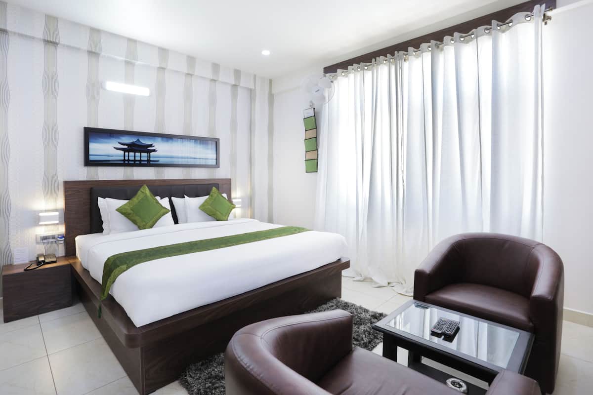 Una habitación de hotel con una cama, una silla, una mesita de vidrio y un cuadro en la pared.
