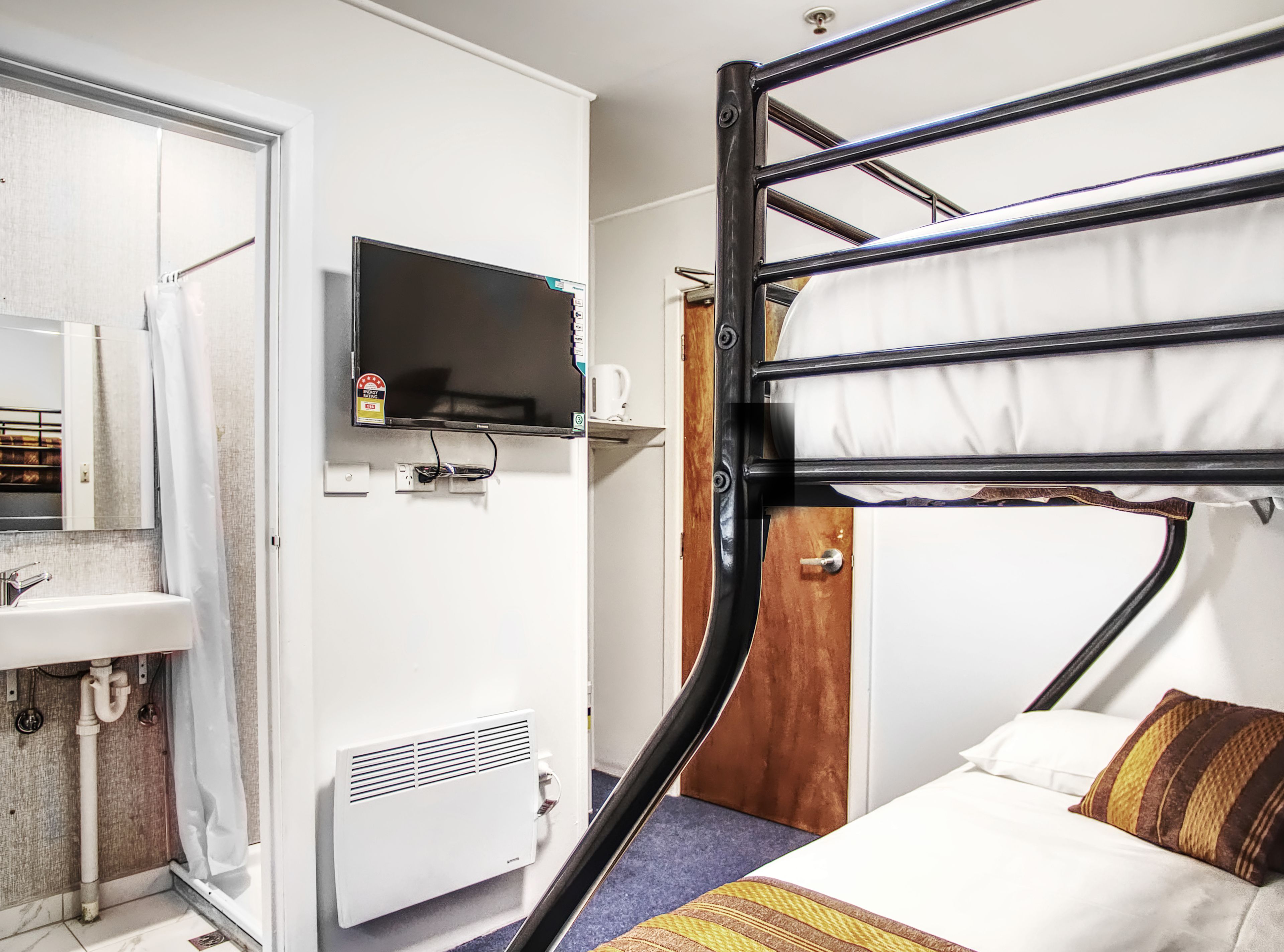 A bunk bed with a television above it, a sink, and a radiator in a room with white walls.