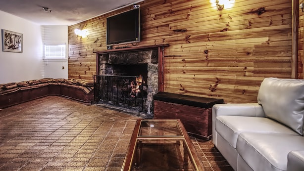 Una sala de estar con chimenea, paneles de madera, televisor y sofá de cuero blanco.