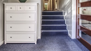 Un pasillo con un aparador blanco, un florero verde y una escalera que lleva a otra habitación.