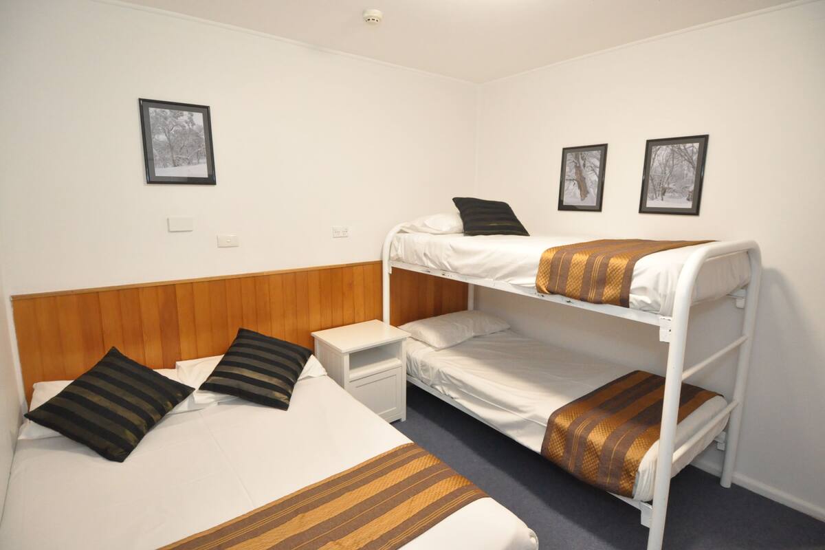 A bunk bed room with a wooden headboard, a nightstand, and two framed pictures on the wall.