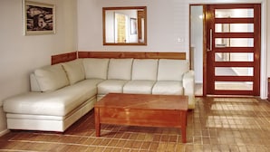 Una sala de estar con un sofá de cuero blanco, una mesa de centro de madera, un espejo con marco de madera y una puerta de madera con mecanismo corredizo.
