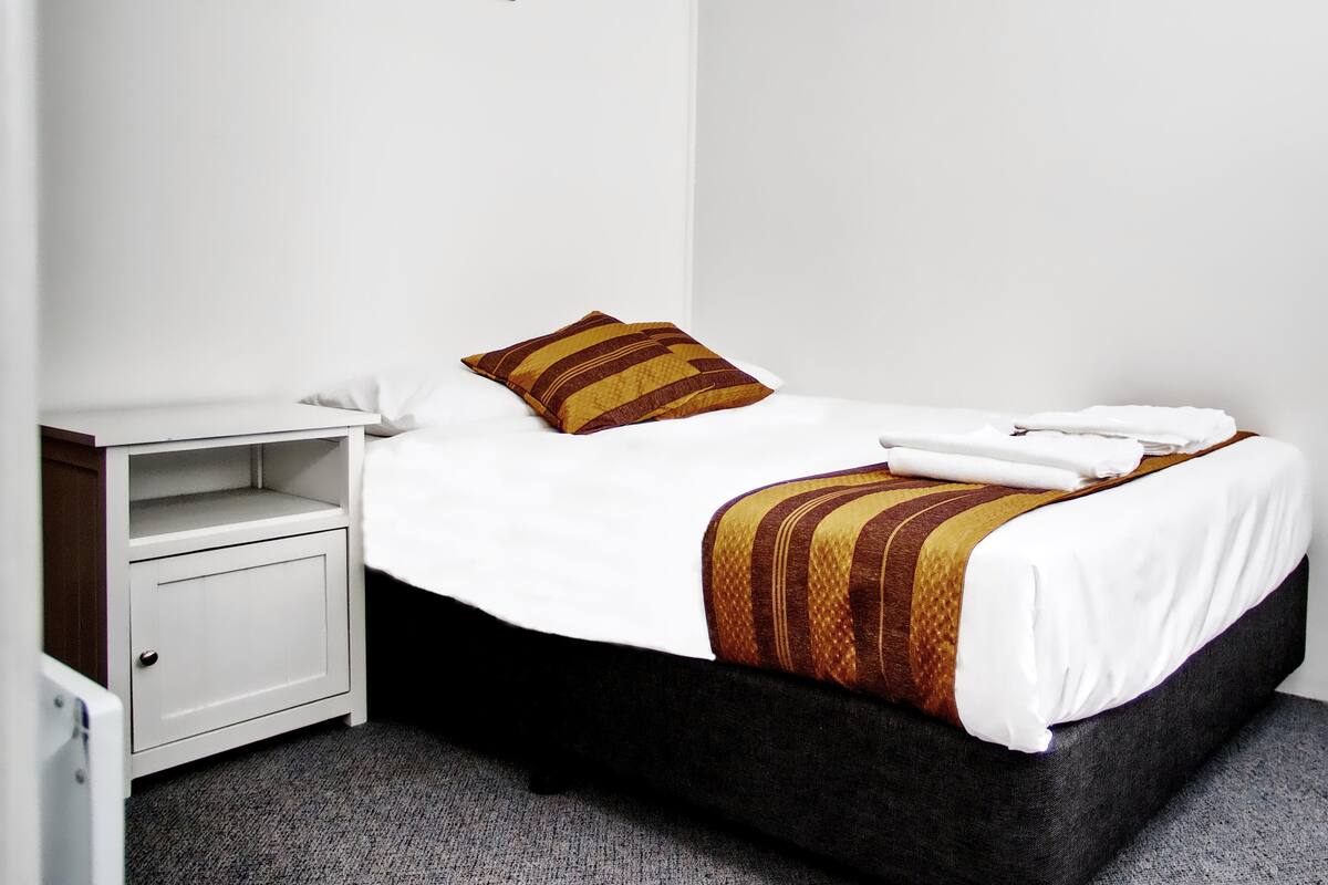 A neatly made bed with white linens and a striped blanket, a small bedside table with a phone, and a framed picture on the wall.
