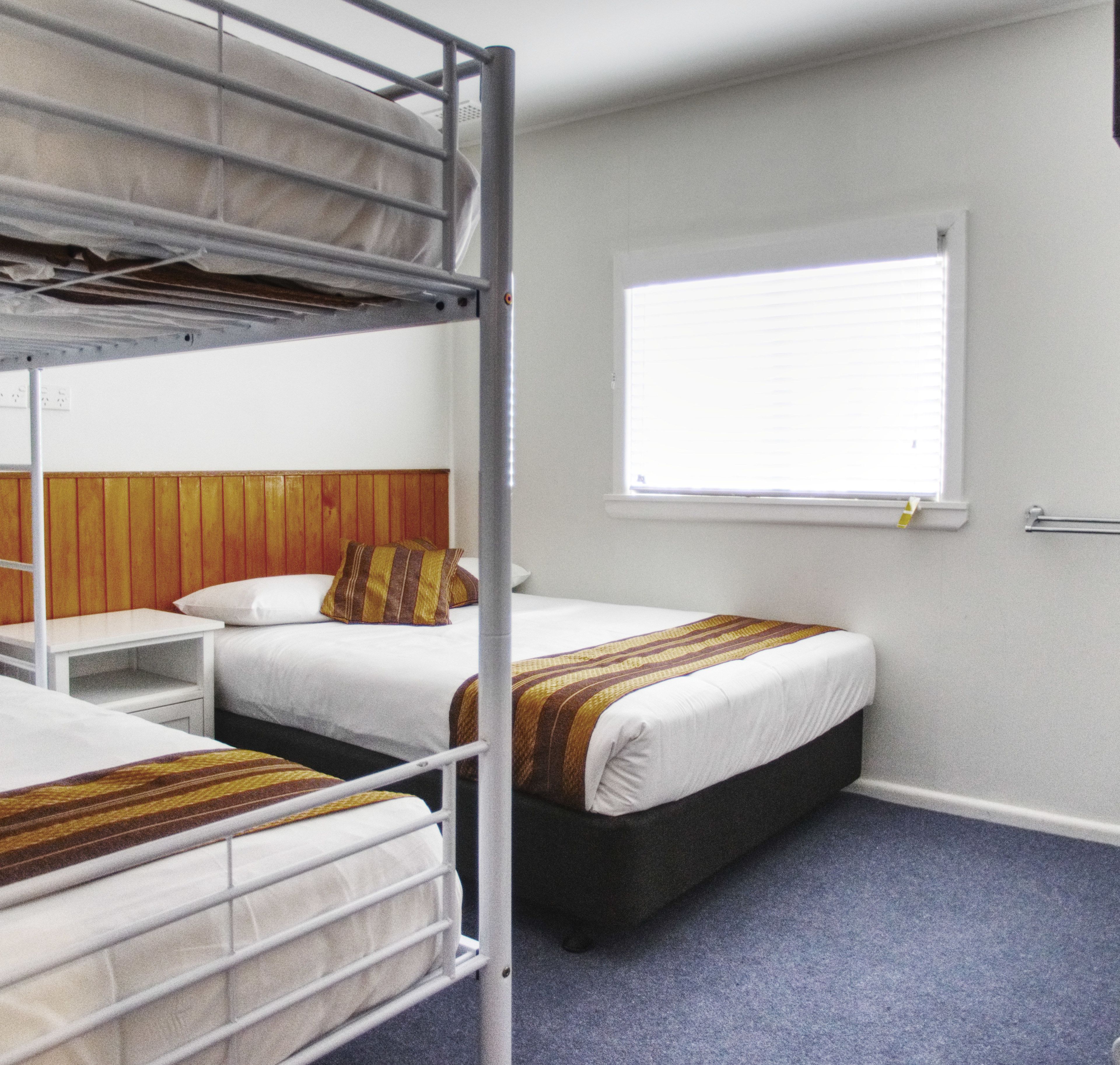 A dormitory room with bunk beds, a window with blinds, and a wooden headboard.