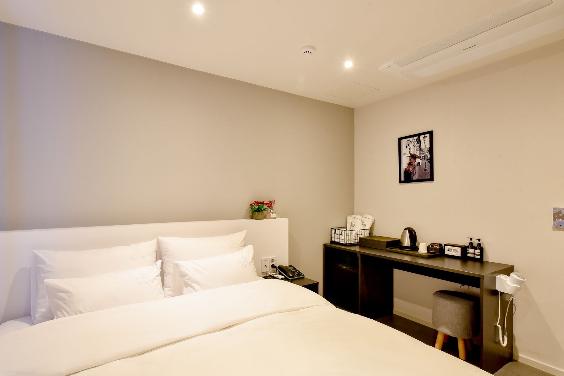 A hotel room with a bed, a desk, a chair, a phone, a hairdryer, and a picture on the wall.
