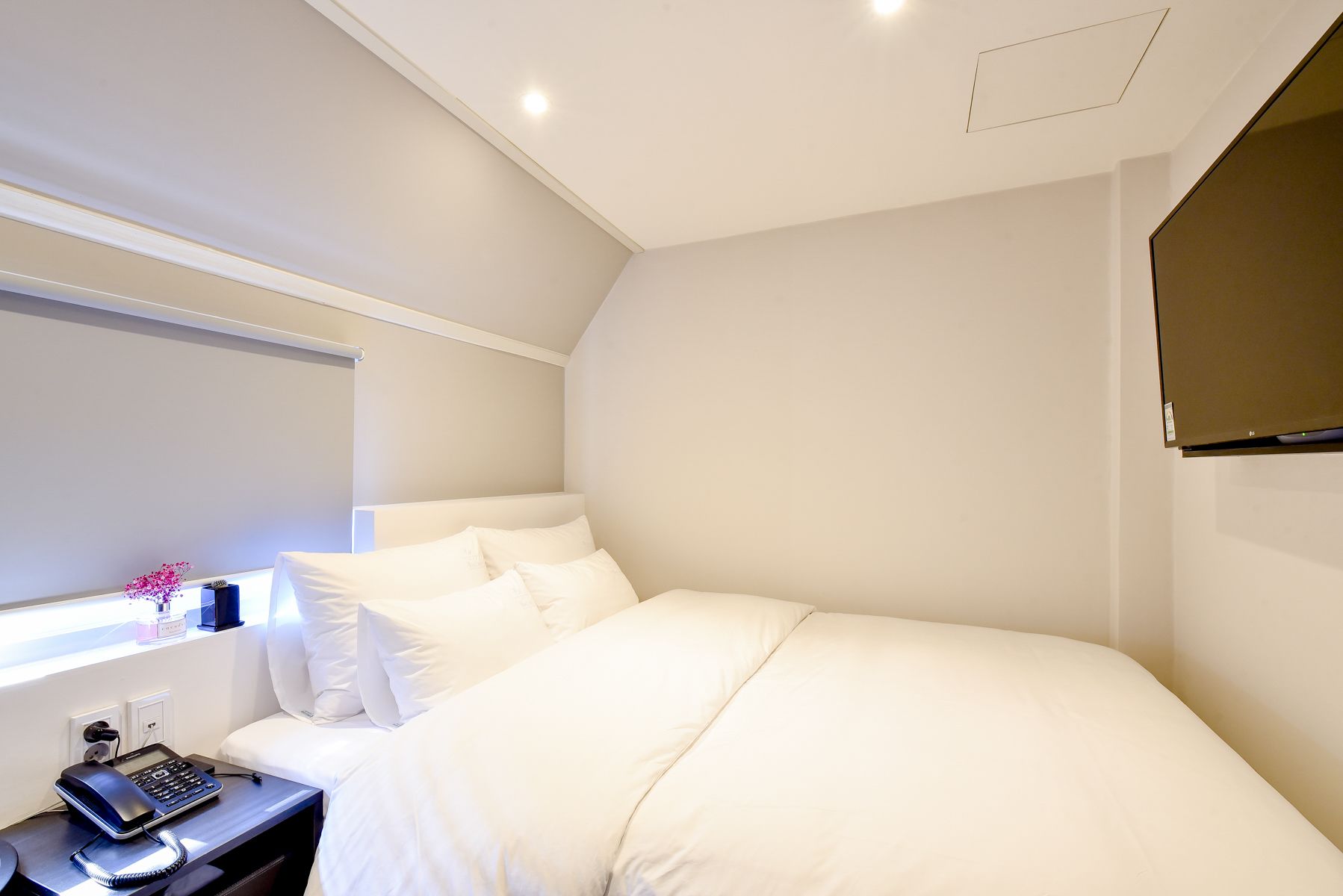 Ein modernes Hotelzimmer mit einem großen Bett, einem Nachttisch mit Telefon und einem kleinen Fenster mit Blick.