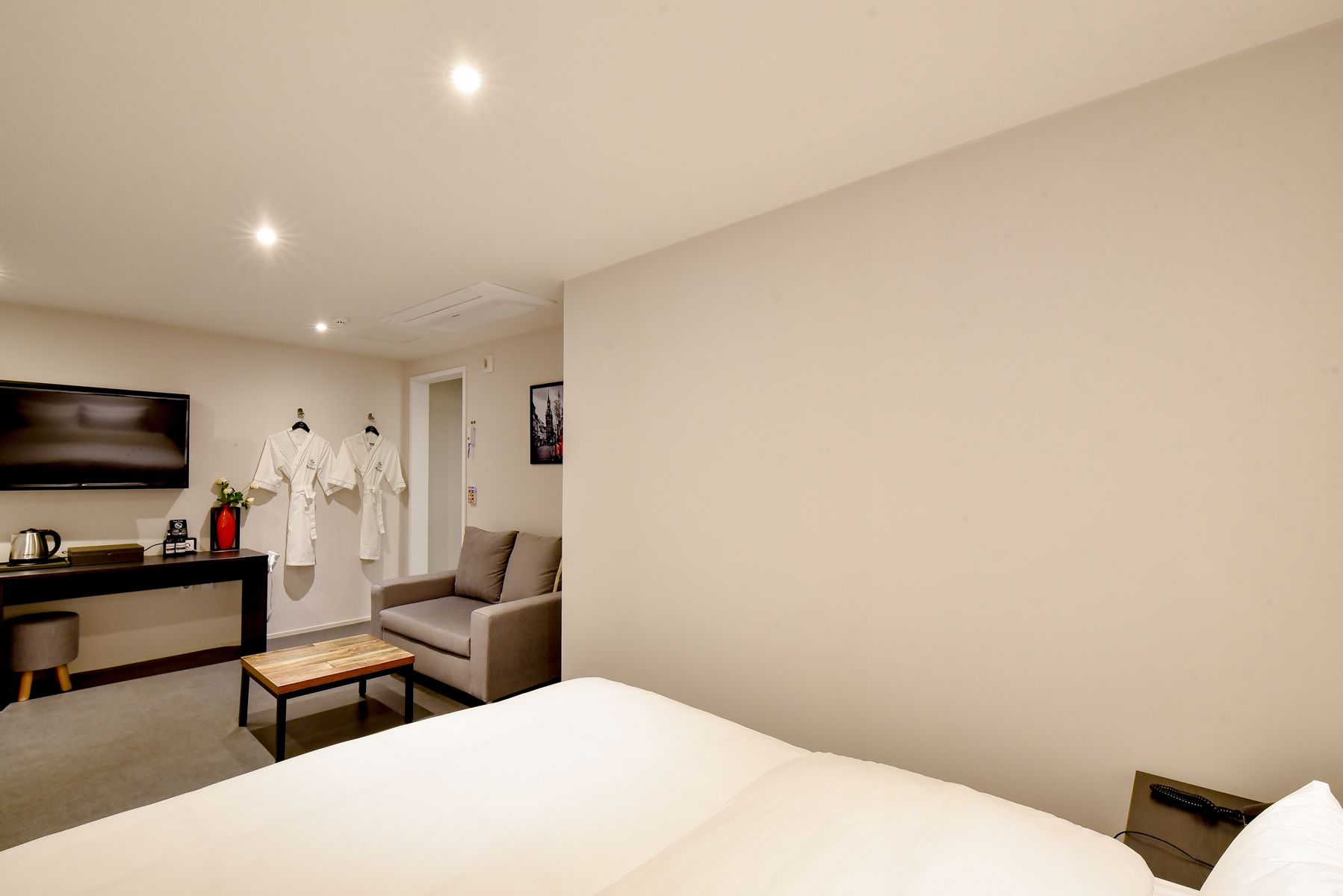 A hotel room with a bed, a desk with a flat-screen TV, a chair, and a small table.