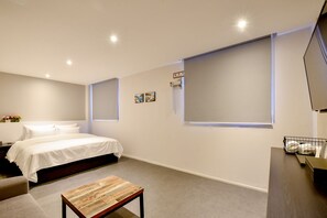 Un dormitorio moderno con una cama, una mesita pequeña y un ventanal grande.