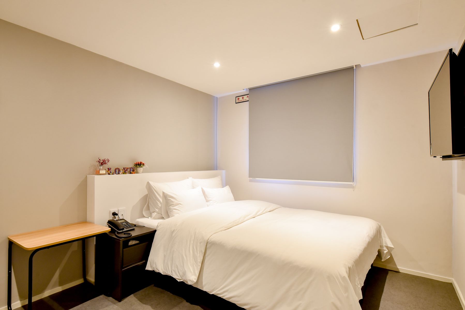 A bedroom with a bed, bedside table, and a wall-mounted TV.