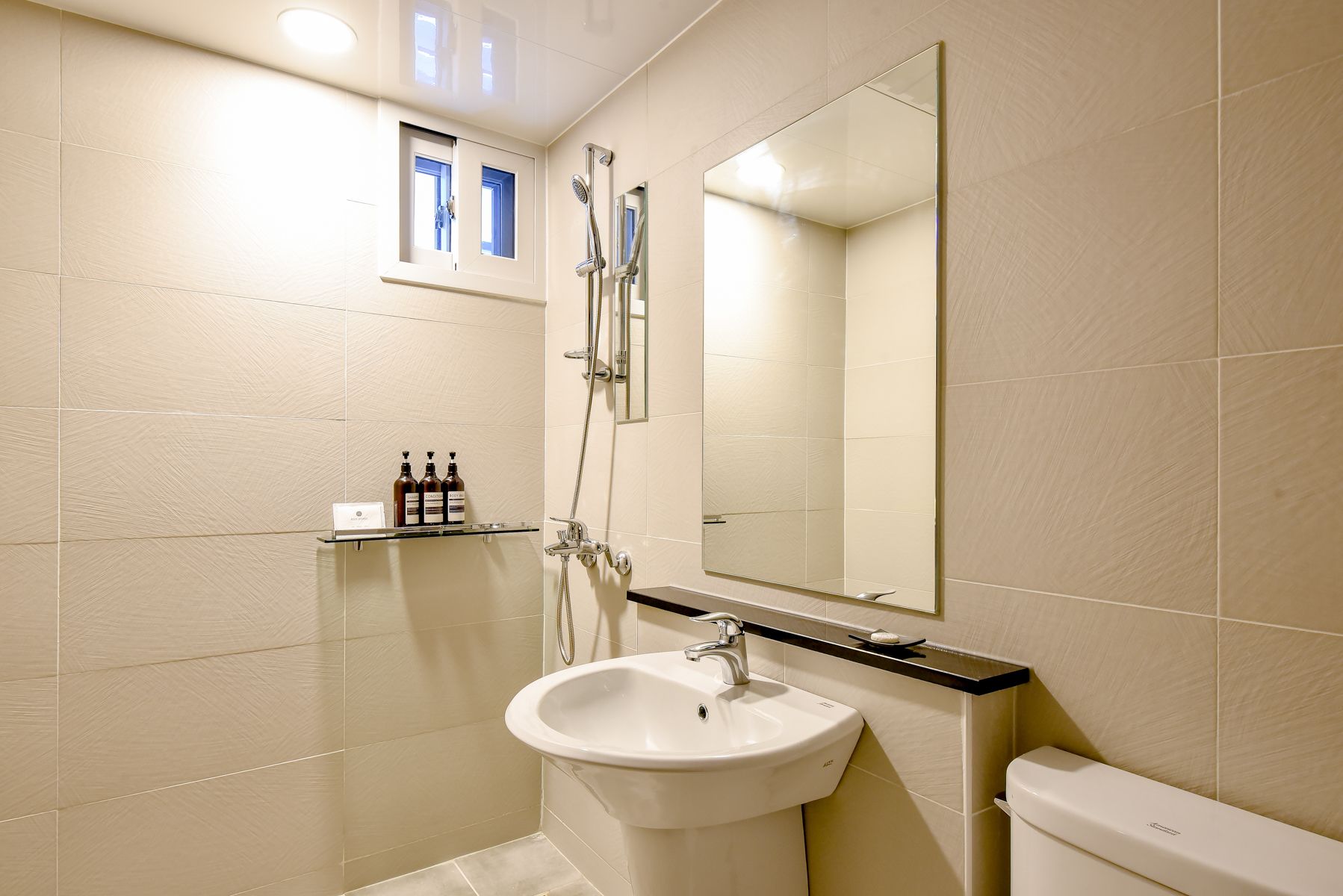 Un bagno con un lavandino bianco, uno specchio e una doccia. Prodotti da bagno su uno scaffale.